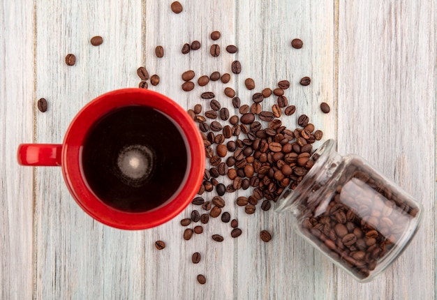 Free Photo top view of cup of coffee and coffee beans spilling out of glass jar on wooden background