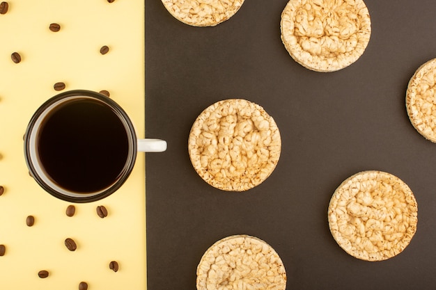 A top view cup of coffee with brown coffee seeds and round crackers