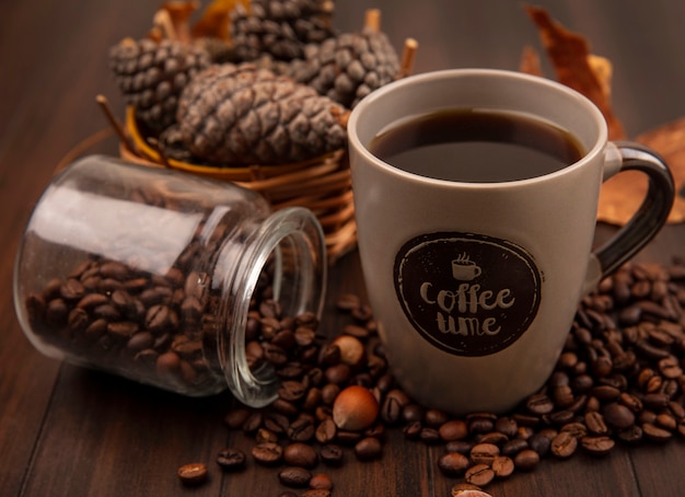 Free photo top view of a cup of coffee with pine cones on a bucket with coffee beans falling out of glass jar on a wooden surface