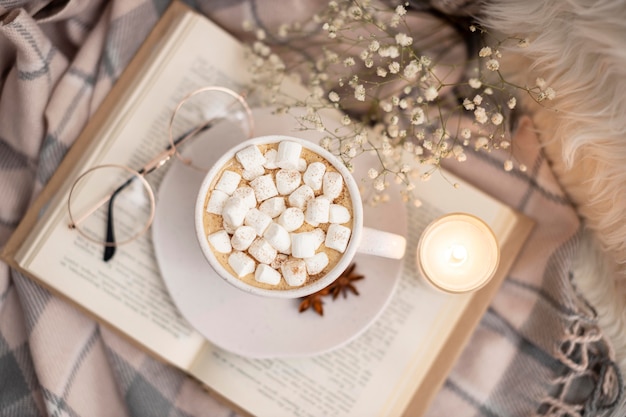 Free photo top view of cup of hot cocoa with marshmallows on book with glasses and candle