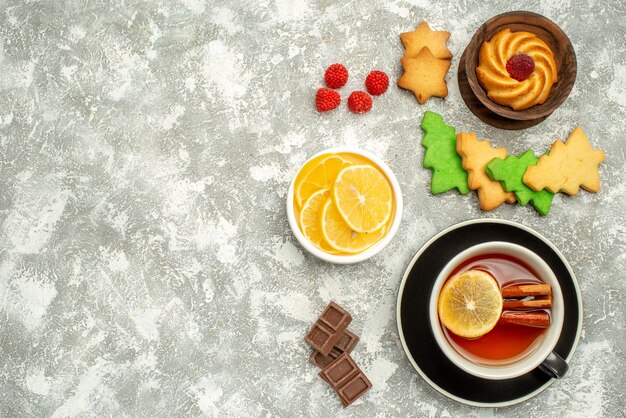 Top view cup of tea biscuit and lemon slices in bowls xmas tree cookies on grey surface free space