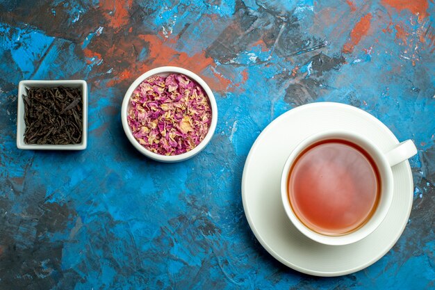 Top view a cup of tea bowls with dried flower petals and tea on blue red surface