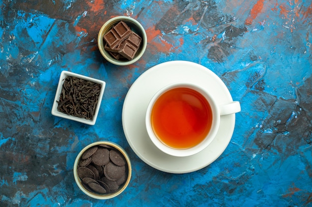 Top view a cup of tea chocolates in small bowls on blue red surface