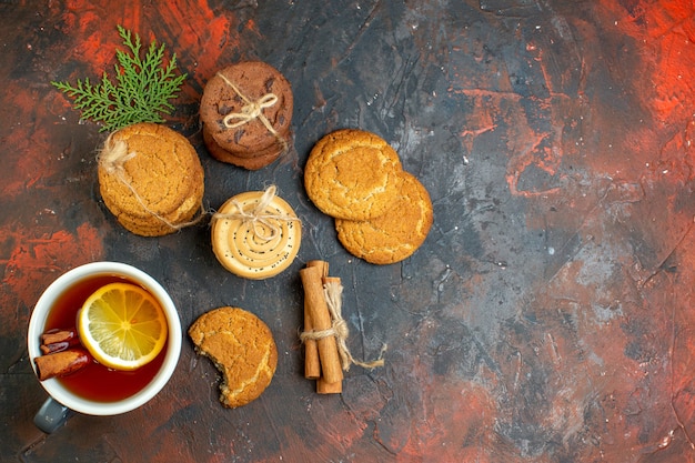 Top view cup of tea cinnamon sticks different cookies tied with rope on dark red table free space