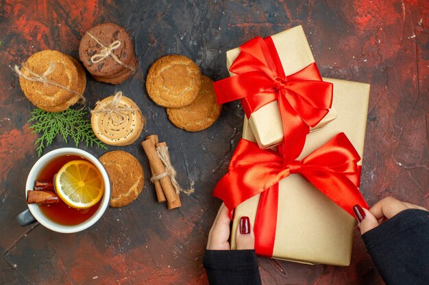 Top view cup of tea cinnamon sticks different cookies tied with rope present in female hand on dark red table