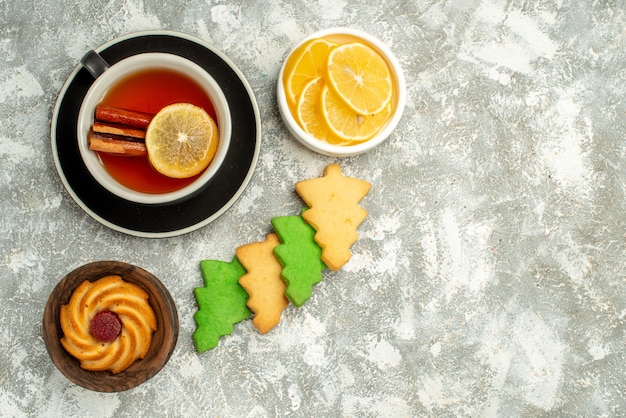 Top view cup of tea cookies lemon slices on grey surface copy space