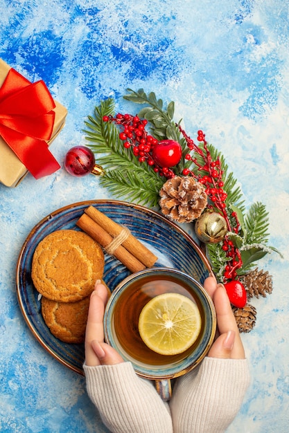 Top view cup of tea in female hand lemon slices cinnamon sticks biscuits in saucer on blue table