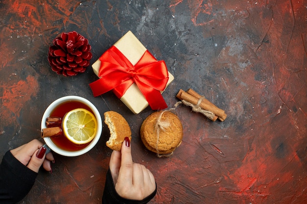 Top view cup of tea flavored by lemon and cinnamon on dark red table