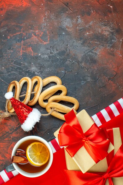 Top view cup of tea flavored by lemon and cinnamon on red tablecloth oval bagels santa hat on dark red table