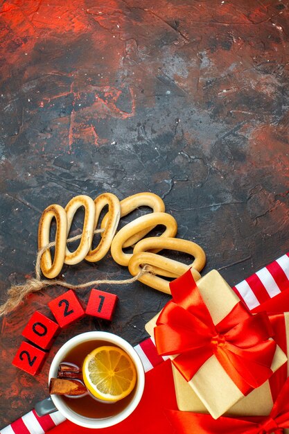 Top view cup of tea flavored by lemon and cinnamon on red tablecloth wood blocks oval bagels gift on dark red background