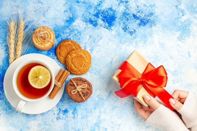 Top view cup of tea gift on female hand on blue table free space