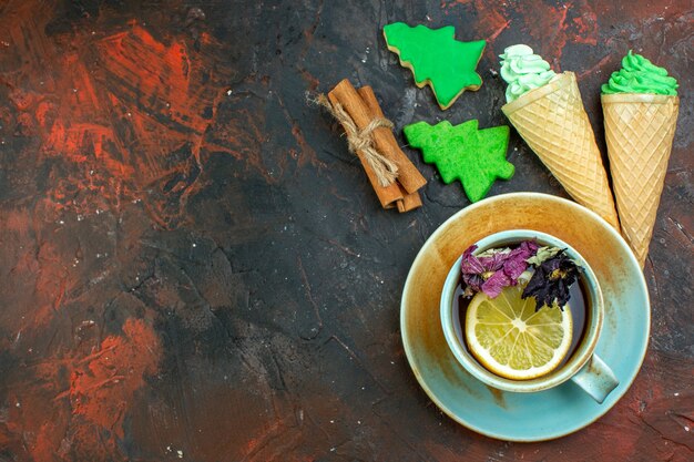 Top view cup of tea ice creams cinnamon sticks xmas tree cookies on dark red table free place