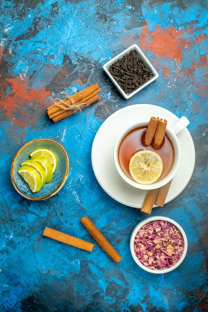 Free photo top view a cup of tea lemon slices cinnamon sticks on blue red surface