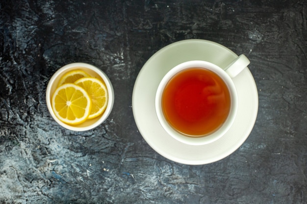 Top view cup of tea lemon slices in small saucer on dark table