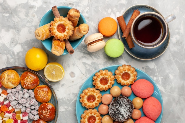 Top view cup of tea with cakes cookies and macarons on white surface