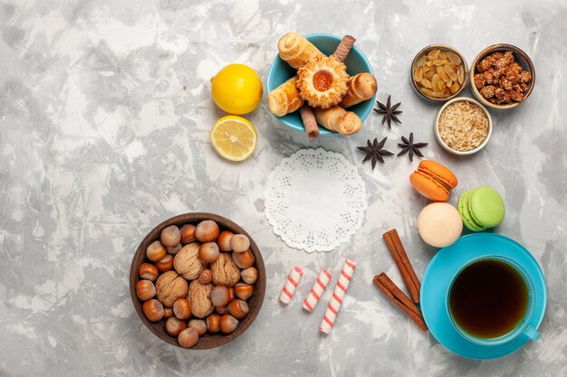 Top view cup of tea with cakes and nuts on white surface