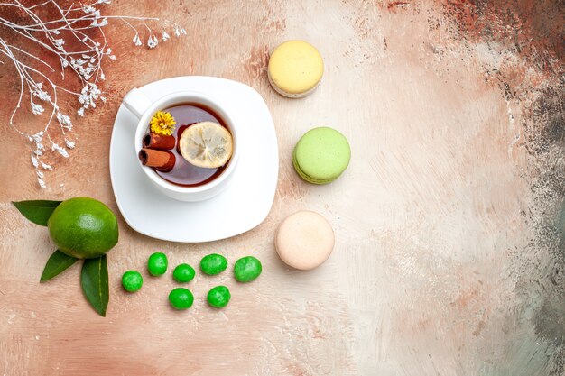 Top view cup of tea with candies and macarons on light table tea lemon biscuit