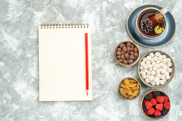 Top view cup of tea with candies and notepad on white space