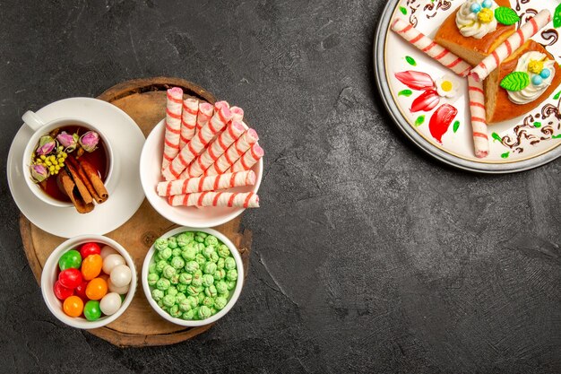 Top view cup of tea with candies and pie slices on dark space