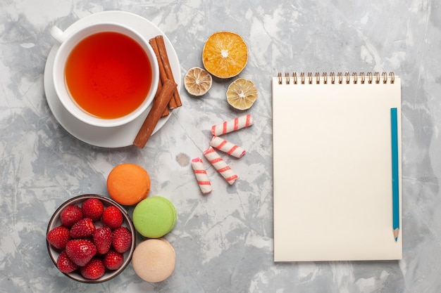 Top view cup of tea with cinnamon and french macarons on white surface