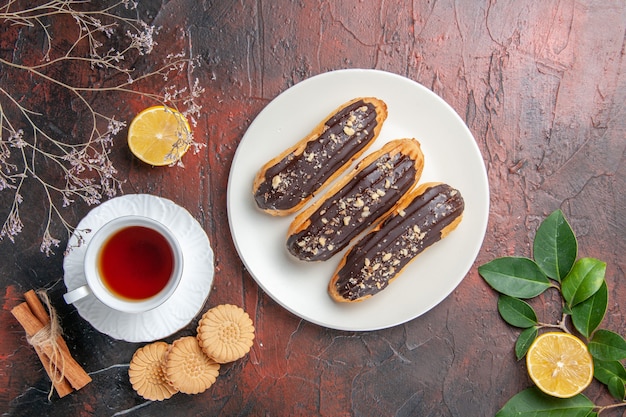 Free photo top view cup of tea with cookies and eclairs on dark table sugar tea biscuit sweet