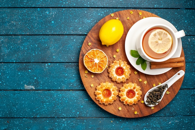 Free photo top view cup of tea with cookies and lemon on a blue desk