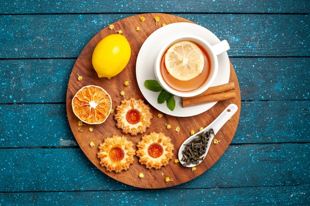 Free photo top view cup of tea with cookies and lemon on blue desk