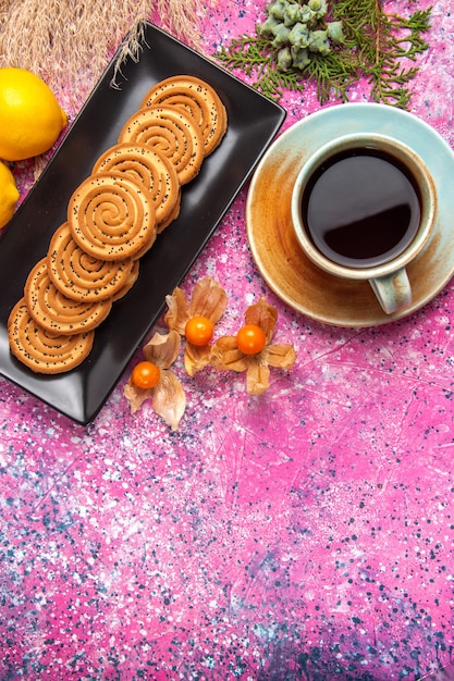 Top view cup of tea with cookies and lemon on light-pink desk.