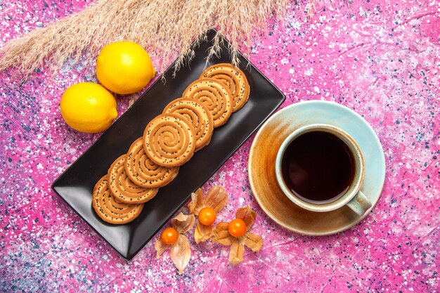 Top view cup of tea with cookies and lemon on pink desk.