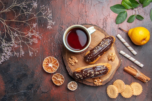 Top view cup of tea with delicious choco eclairs on dark table cake sweet dessert