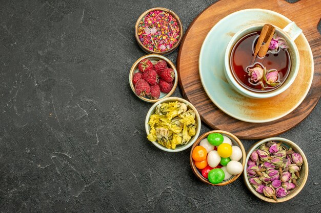 Top view cup of tea with flowers and candies on the grey space