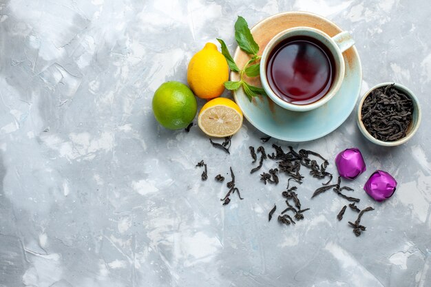 Top view cup of tea with fresh lemons candies and dried tea on white table, tea fruit citrus