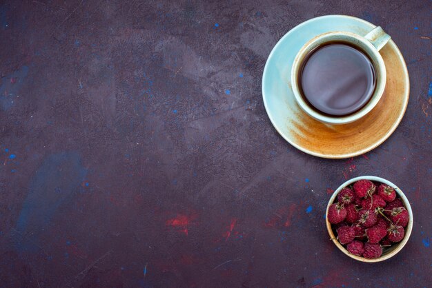 Top view of cup of tea with fresh raspberries on dark surface