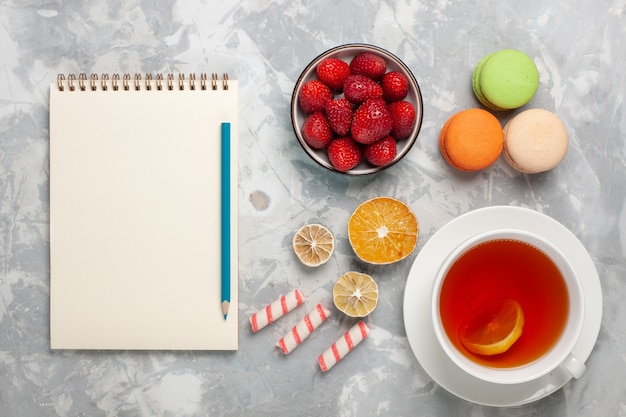 Top view cup of tea with fresh red strawberries and french macarons on white desk