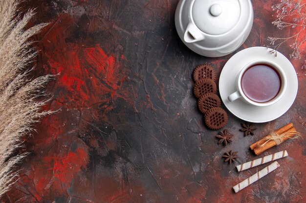 Top view cup of tea with kettle and cookies on the dark table