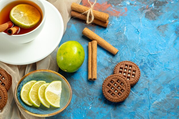 Top view cup of tea with lemon and cinnamon beige shawl biscuits lemon on blue red table copy place