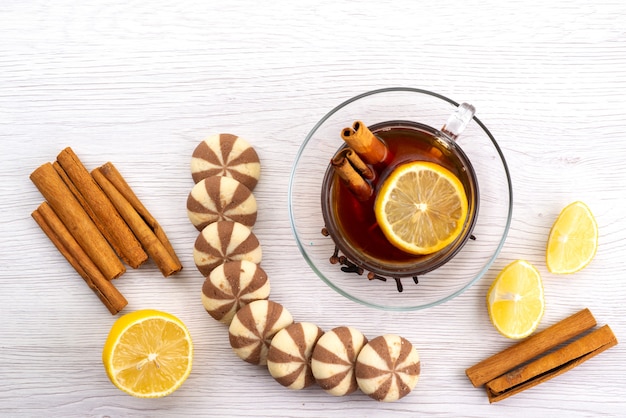 A top view cup of tea with lemon cookies and cinnamon on white, tea dessert candy