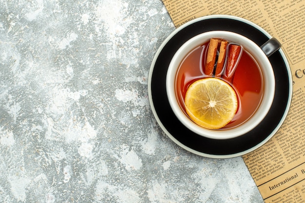 Top view a cup of tea with lemon slices and cinnamon sticks on newspaper on grey surface copy place