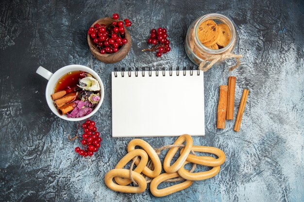 Top view of cup of tea with red cranberries and crackers on dark surface