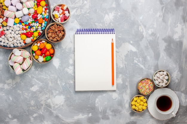 Top view cup of tea with sweet confitures and notepad on white desk