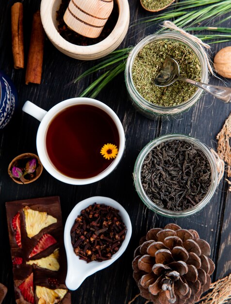 Top view of a cup of tea with various spices and herbs in glass jars on rustic