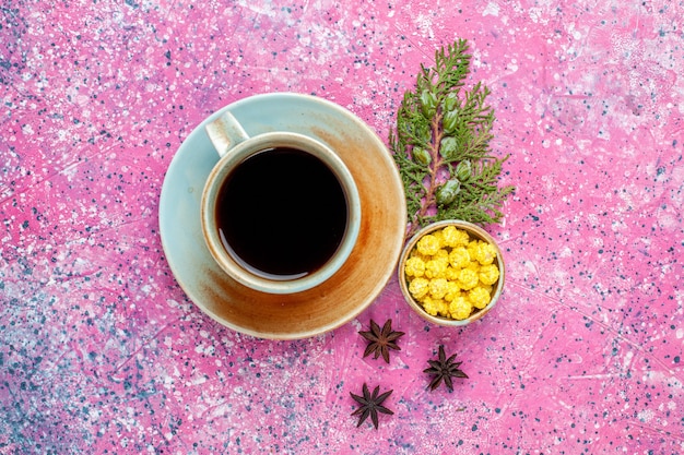 Top view cup of tea with yellow candies on pink desk