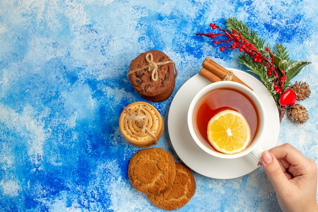 Top view cup of tea in woman hand cookies tied up with rope on blue table copy place