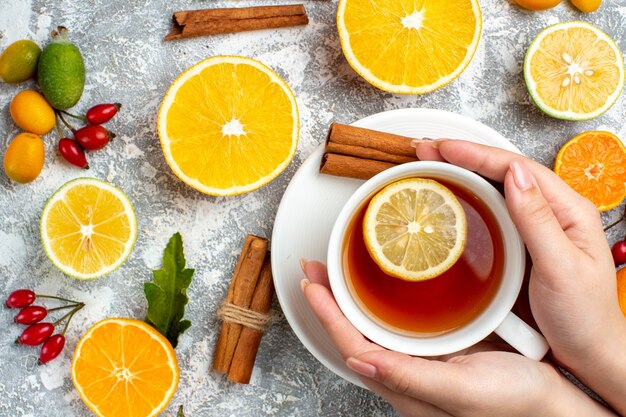 Top view a cup of tea in woman hands cut lemons cinnamon sticks on grey background