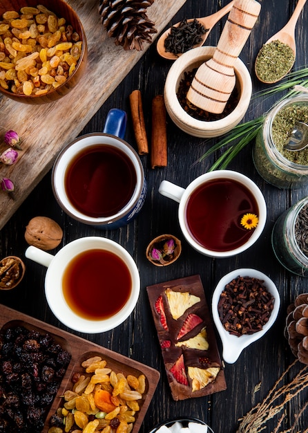 Top view of cups of tea and various spices and herbs with mixed nuts and dried fruits on rustic