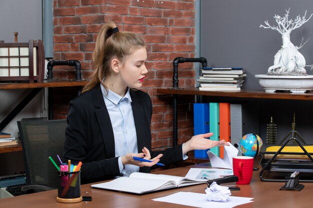 Top view of curious lady sitting at a table and focused on something carefully in the office