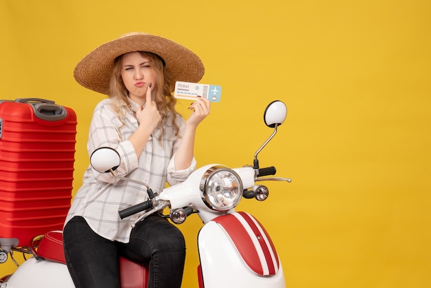 Top view of curious young woman wearing hat and sitting on motorcycle and holding ticket on yellow 