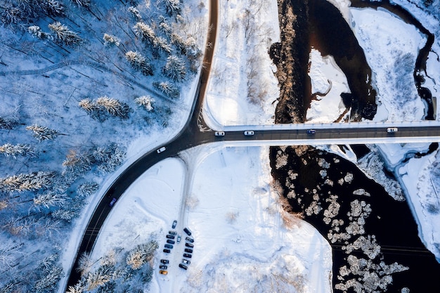 Top view of a curvy road over a flowing river through the snow-covered forest