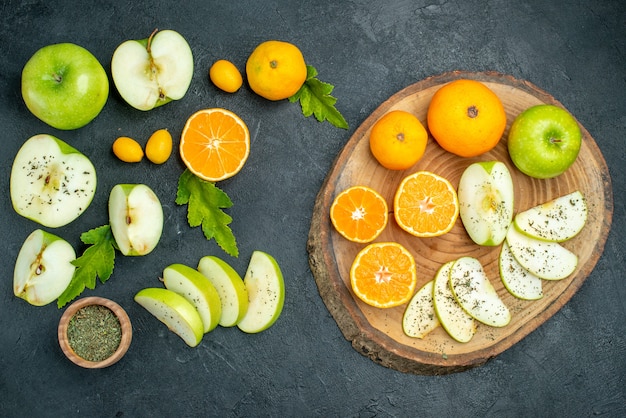 Free Photo top view cut apples and mandarines on round board leaves cumcuat dried mint powder in bowls on dark table