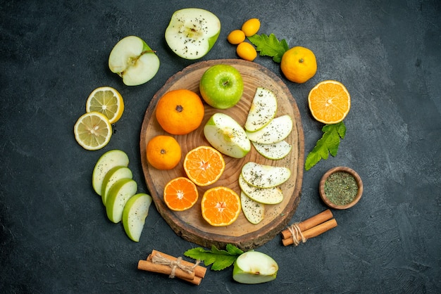 Top view cut apples and mandarines on rustic round board cinnamons tied with rope cumcuat and other stuffs around board on dark table